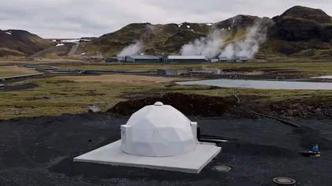 A white dome in foreground and steam over the carbon capture plant in the distance