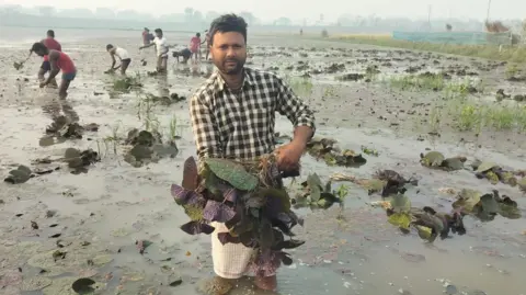 Dhirendra Kumar Dhirendra Kumar standing in a flooded field holding a lily plant