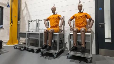 Chris Baraniuk Crash test dummies sit on trolleys wearing orange jerseys.