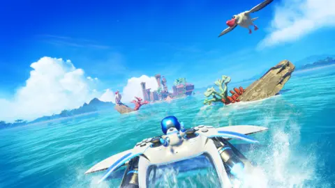 Team Asobi A screenshot shows Astro Bot clinging to a flying PS5 controller as it swoops close to the surface of the sea, throwing spray up into the air. Rocky obstacles line the route to his destination - a distant island with a wrecked ship on its shore.