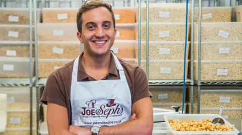 Joe & Seph’s popcorn Adam Sopher, co-founder and chief executive of Joe & Seph’s popcorn, sitting in front of a selection of tubs of popcorn