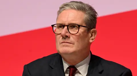 Sir Kier Starmer wearing a suit with a white shirt and red tie against a red and white background