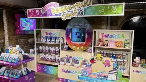 The Tamagotchi shop features a display with a massive tamagotchi in the back, and lots of the devices on many shelves