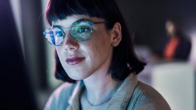 A business person looking at charts on a computer with light reflecting off their glasses.