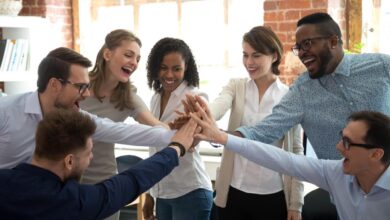 Several people putting their hands together in the middle of a huddle in an office.