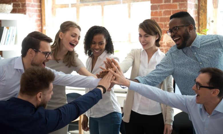 Several people putting their hands together in the middle of a huddle in an office.