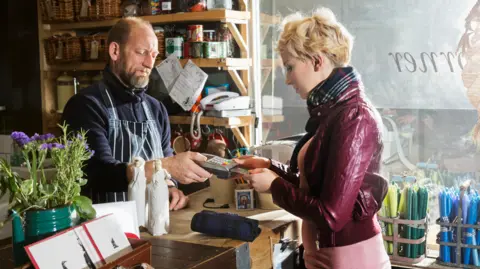 Getty Images Male shop keeper serves young woman