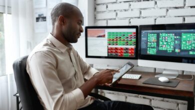 Person sitting at desk, stock screens on the desktop monitors, looking at phone.