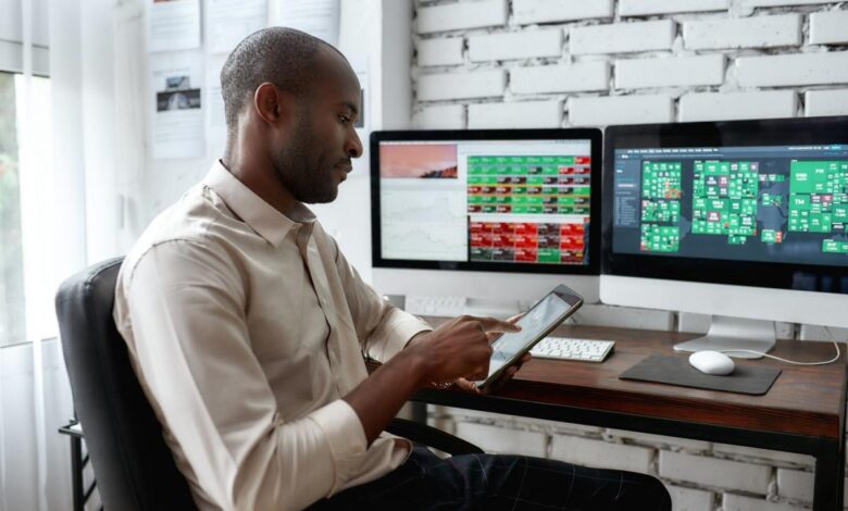 Person sitting at desk, stock screens on the desktop monitors, looking at phone.