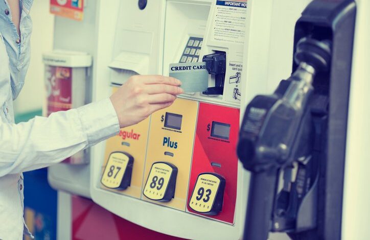 A hand placing a credit card into a gas pump card reader.