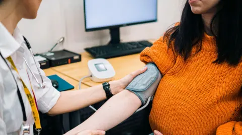 Getty Images A GP measuring the blood pressure of a woman in a doctor's office