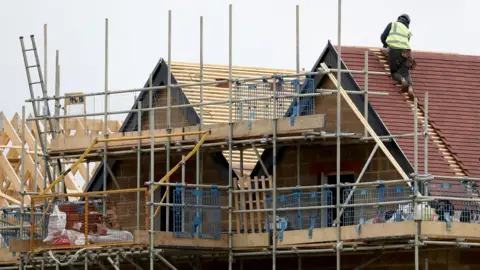 PA Media Builder wearing a high-vis jacket and a hard hat working on a roof of a house under construction