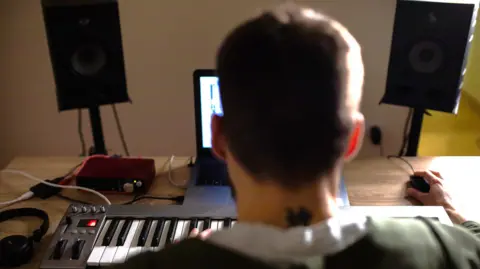 Getty Images Stock image of a rear view of a musician sitting at a desk in front of a keyboard using his computer