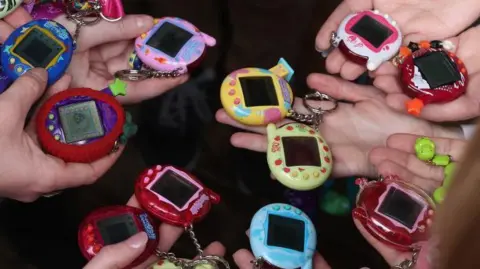 Getty Images Tamagotchi in lots of different colours.  They are small egg-shaped devices with a digital screen in the middle and three buttons underneath. The colours range from a deep see-through red to bright blue, green, yellow and purple.