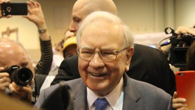 Warren Buffett smiling, surrounded by cameras.