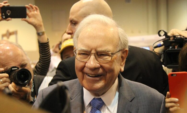 Warren Buffett smiling, surrounded by cameras.