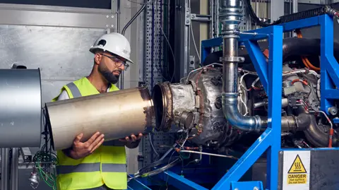 Ross Jarman Ihab Amed working on the test jet engine. He's connecting a metal tube to another piece of equipment.