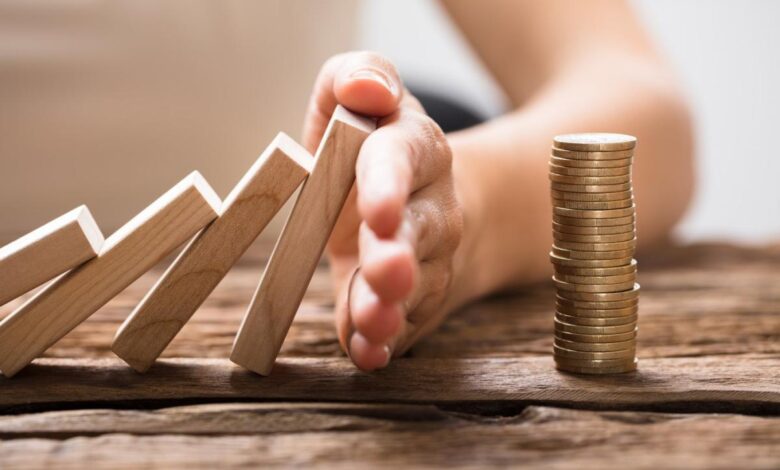 A hand stopping falling dominos from overturning a stock of coins.