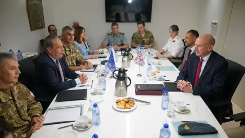 PA Vasilis Palmas and John Healey sitting around a white table with various military generals