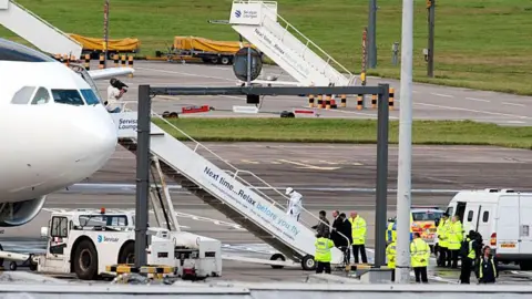 AFP Abdelbaset Ali Mohmet al-Megrahi walks up the steps to board an aircraft at Glasgow airport on 20 August 2009. He is followed by three men in suits and police officers and other people in high vis clothing can be seen on the tarmac.