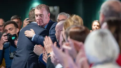 Plaid Cymru Rhun ap Iorwerth embracing former Plaid Cymru leader Adam Price surrounded by supporters at Plaid Cymru conference.