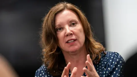 PA A head and shoulders image of Dame Rachel de Souza mid-speech. She has wavy brown hair worn loose to her shoulders and is wearing a navy blue coloured blouse with white polka dots.