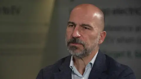 Head and shoulders shot of Dara Khosrowshahi wearning an open-neck shirt