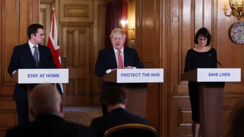 Getty Images Robert Jenrick with Boris Johnson and Deputy Chief Medical Officer for England Jenny Harries deliver a Covid briefing to journalists at Downing Street in March 2020 