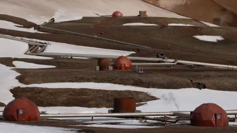 Steel pipes zig-zag across the Icelandic landscape connecting red pods of a geothermal power station