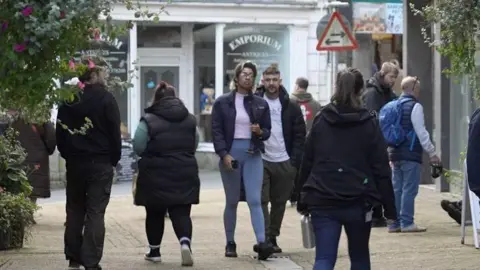 Shoppers in Liskeard, Cornwall, with a young man and women dressed in casual clothing in the centre of the frame