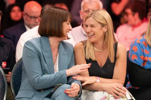 PA Rachel Reeves (left) and her sister Ellie Reeves seen laughing together, sitting next to each other at a campaign rally 