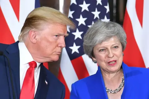 AFP Donald Trump, in red tie and navy suit, leans towards Theresa May, in bright blue blazer, during his 2019 state visit to the UK. Behind them are UK and US flags