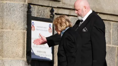 PA Alex Salmond's widow Moira is directed into the church by a man wearing a black suit