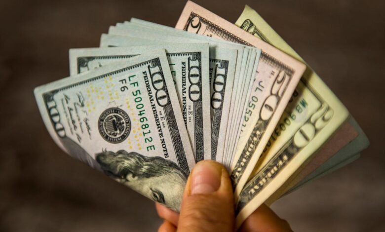 A person holding a fanned and folded assortment of cash bills in their hands.