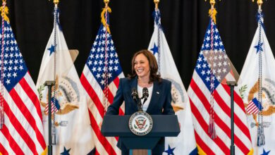 Vice President Kamala Harris standing at a podium in front of flags.