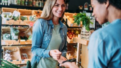 Two people smile while processing a transaction in a store using a credit/debit card reader.