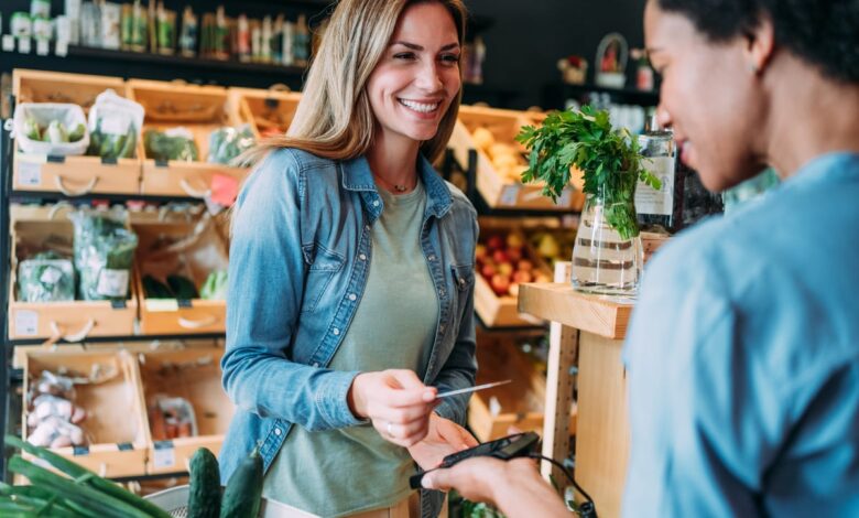 Two people smile while processing a transaction in a store using a credit/debit card reader.