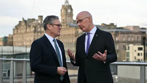 Reuters Sir Keir Starmer and John Swinney talking to each other with Edinburgh in the background. Both men are wearing dark suits, white shirts and ties.