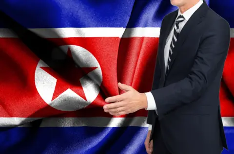 Getty Images A man in a suit offering a handshake, with the North Korea flag in the background