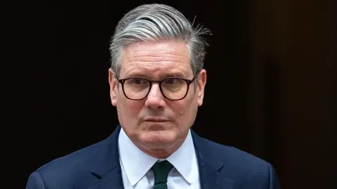 Getty Images Sir Keir Starmer looks to the left of the camera while wearing suit, tie and glasses as he comes out of 10 Downing Street in London