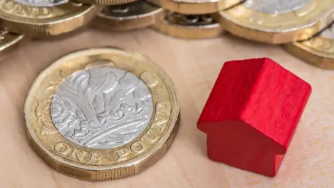 Getty Images A red wooden model of a house next to a pile of UK pound coins