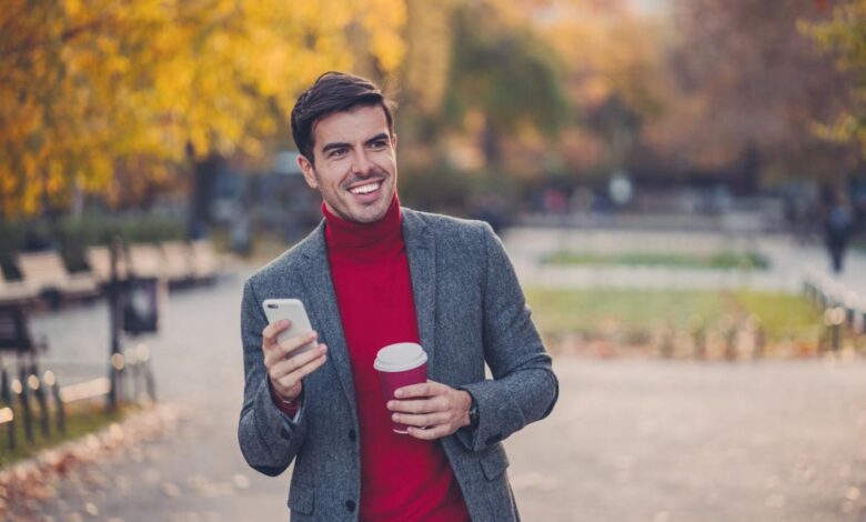 An investor smiles while walking through a park in the fall.