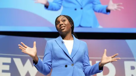 PA Kemi Badenoch wearing a blue jacket standing on stage at the Conservative Party conference this month . 