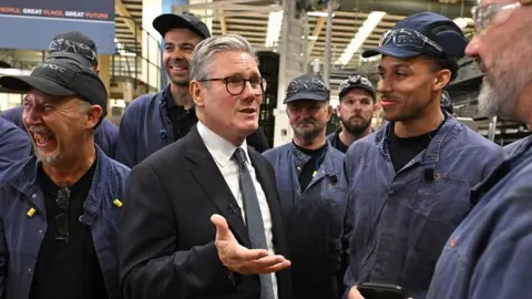 Getty Images Sir Keir Starmer chats to smiling workers in overalls on a visit to a glass factory in Chester