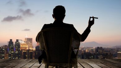 Someone sitting down and holding a cigar while looking towards a skyline.