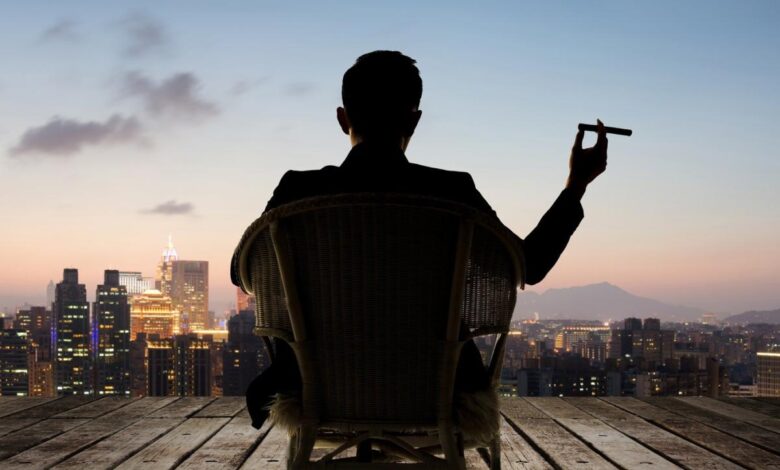 Someone sitting down and holding a cigar while looking towards a skyline.