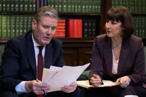 Getty Images Keir Starmer and Rachel Reeves sit in a parliamentary office in front of leatherbound books going through files as they prepare for the Tory Spring Budget in Parliament.