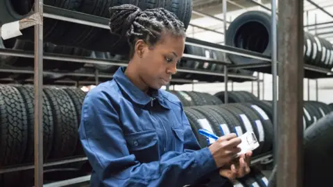 Getty Images Woman writing on a clipboard, standing between rows of tyres