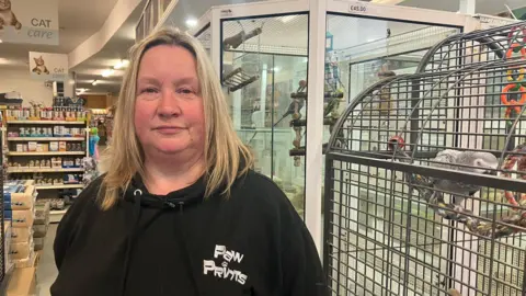 Pet-shop owner Tracey Robertson on the store floor next to a cage displaying a parrot