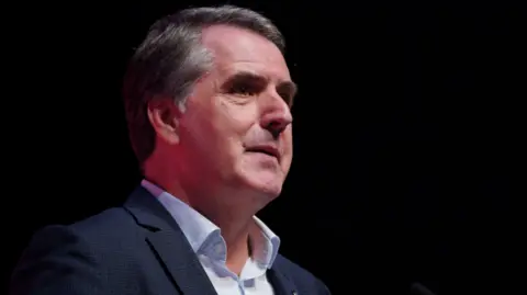 PA Media Mayor of the Liverpool City Region Steve Rotheram, in a blue suit and light blue shirt, standing at a podium delivering a speech